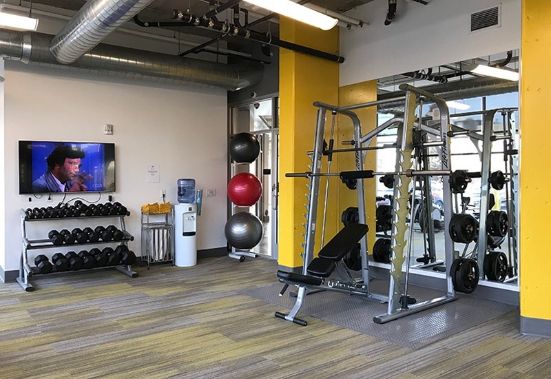 A gym with a variety of equipment including a weight bench, a rowing machine, and a television.