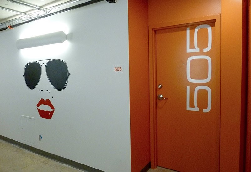 A white wall with a drawing of a woman's face and a door with the number 505 on it.