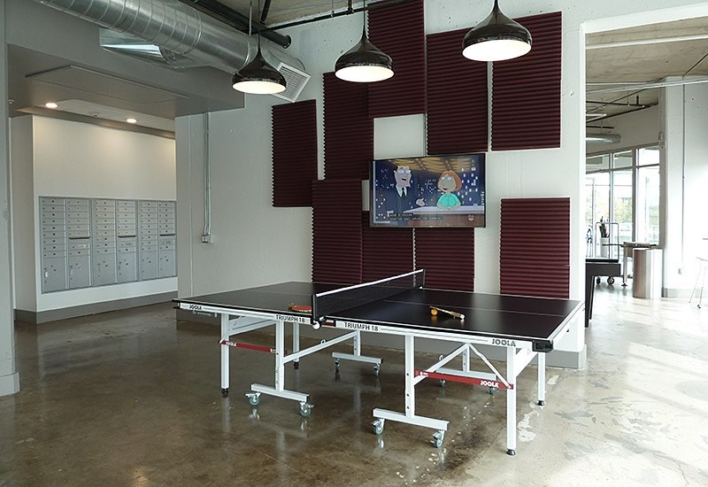 A ping pong table is in the middle of a room with a TV on the wall.
