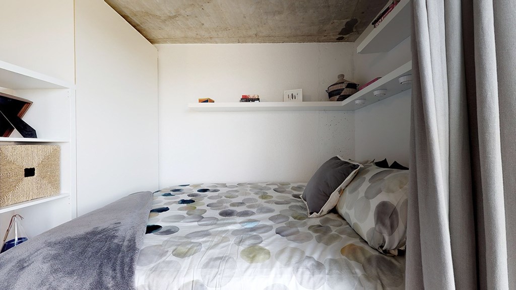 A bed with a grey and white patterned comforter and a grey pillow is in the foreground of the image.