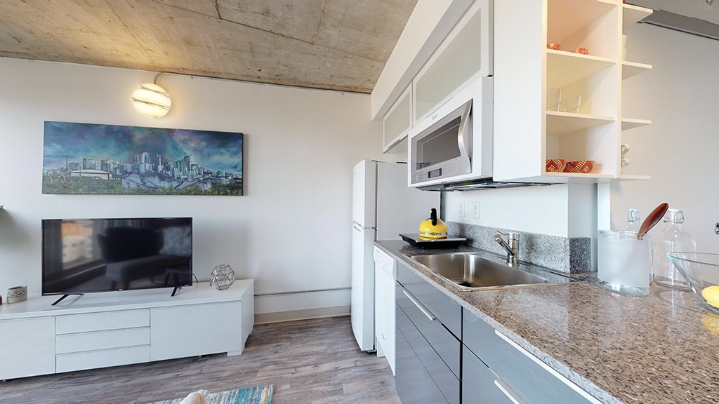 A modern kitchen with a white countertop and a television on the side.