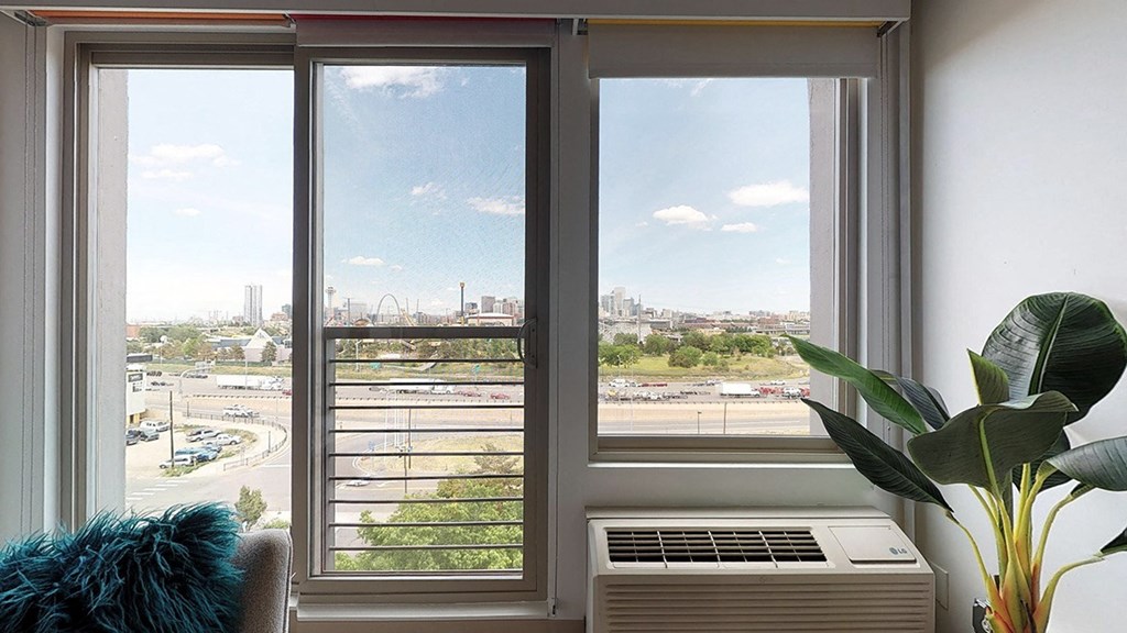 A view of a cityscape through a window with a blue cushion on the left and a plant on the right.