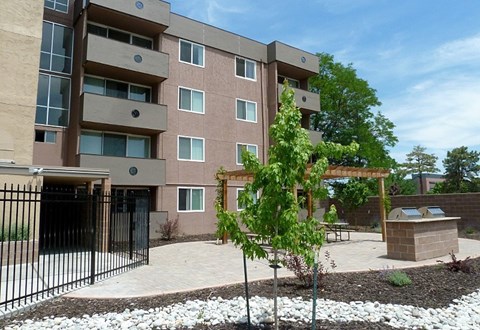 A brown apartment building with a black gate and a small tree in front.