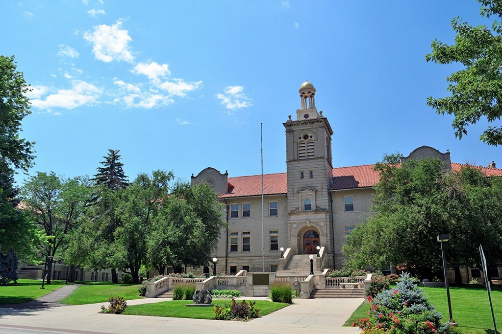 A large building with a tower and a red roof is surrounded by trees and greenery.