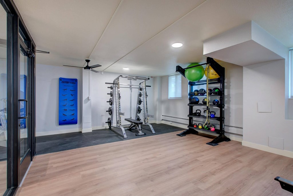A gym room with a variety of equipment including a squat rack, bench, and a wall-mounted rack with multiple resistance bands.
