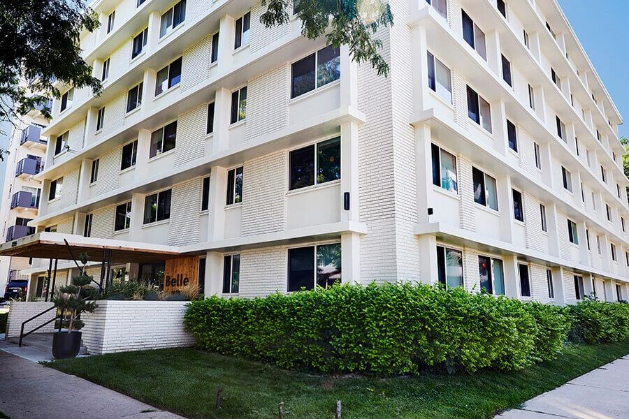 A white building with a green hedge in front.