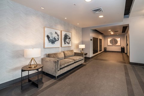 A living room with a grey sofa and a table with a lamp on it.