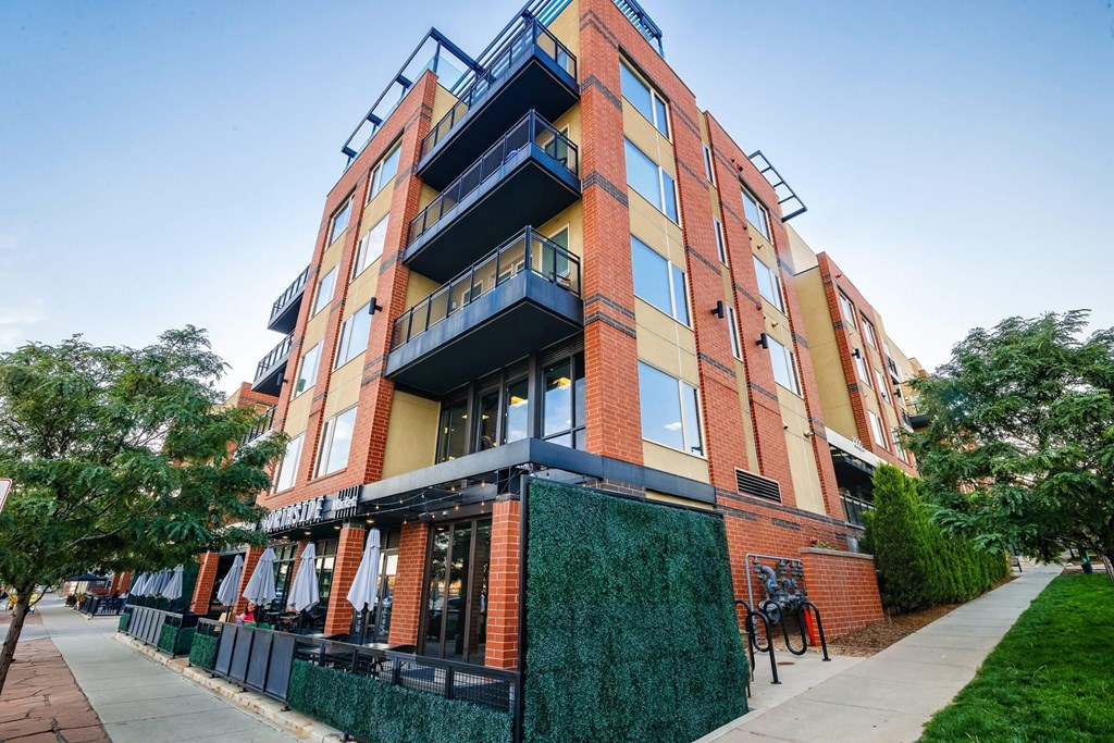 A multi-story building with balconies and a green fence in front.