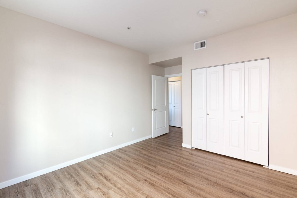 A room with white walls and wooden flooring with a white door on the right.