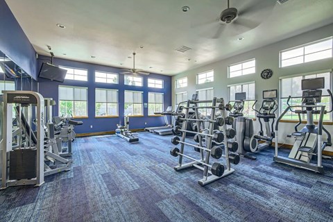 A spacious gym with a variety of equipment and a ceiling fan.
