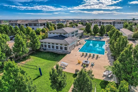 A large swimming pool surrounded by a grassy area and trees with a building in the background.