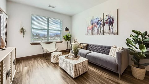 A living room with a grey couch, a white wicker coffee table, and a painting of horses on the wall.