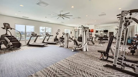 A spacious gym with a variety of equipment and a fan on the ceiling.