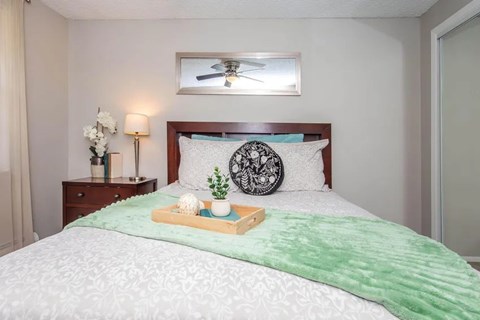 A bedroom with a bed, a nightstand with a lamp, and a ceiling fan.
