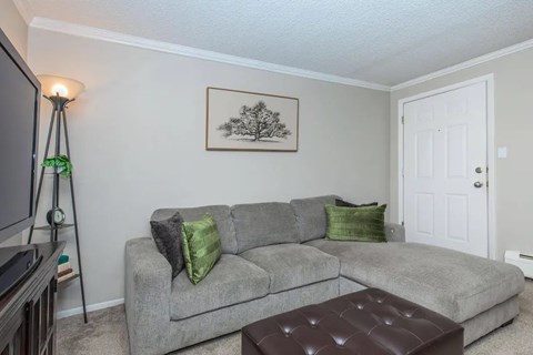 A grey couch with green pillows sits in a living room with a painting on the wall.