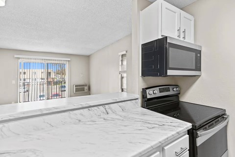A kitchen with a black microwave above a stove and a white counter.