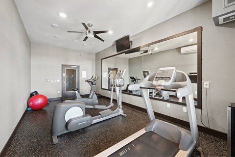 A spacious home gym with a treadmill, elliptical machines, and a mirror.