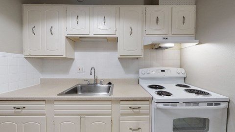 A white stove and sink in a kitchen with white cabinets.
