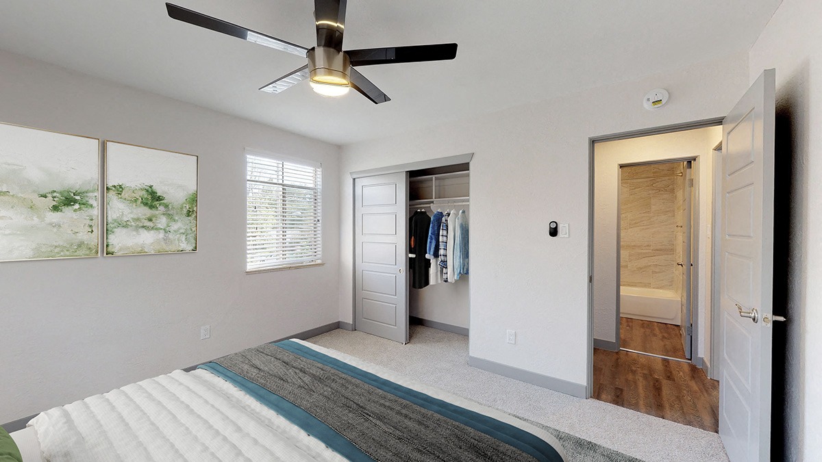A bedroom with a ceiling fan and a bed with a striped rug on the floor.