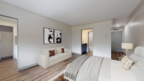A white couch with a brown throw pillow sits in a living room with a white wall and a framed picture above it.