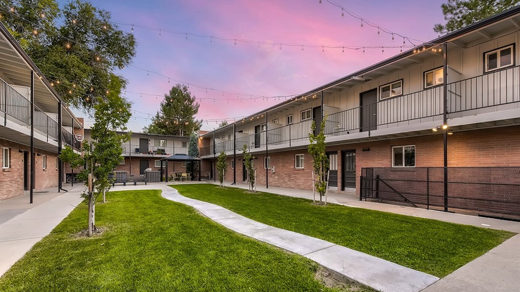 A sunset view of apartment buildings with a green lawn in the foreground.