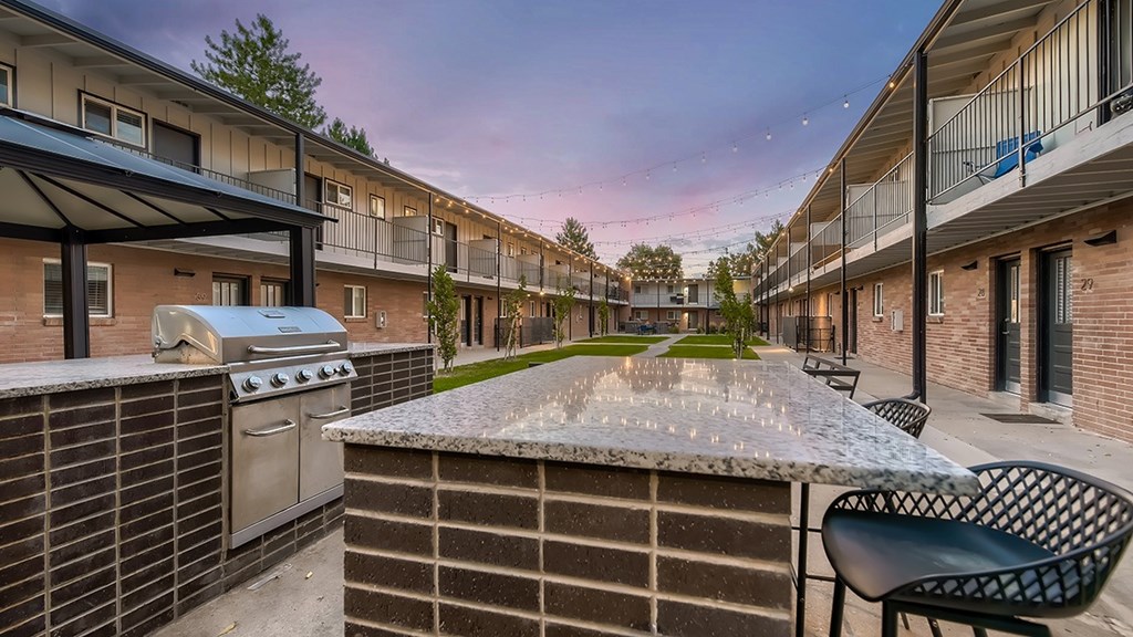 A patio with a grill and chairs is surrounded by apartment buildings.