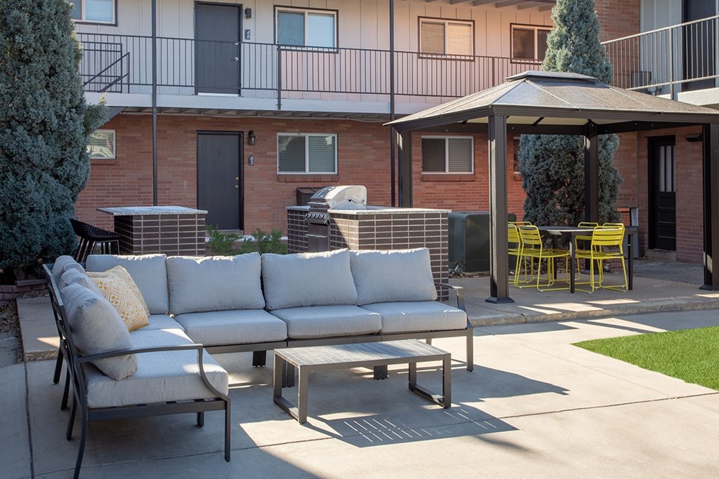 A patio with a white couch, yellow chairs, and a table with a tree in a pot.