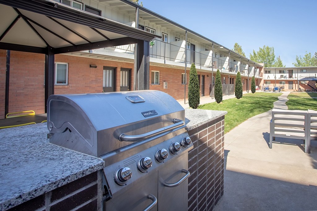 A silver grill is on a patio with a building in the background.