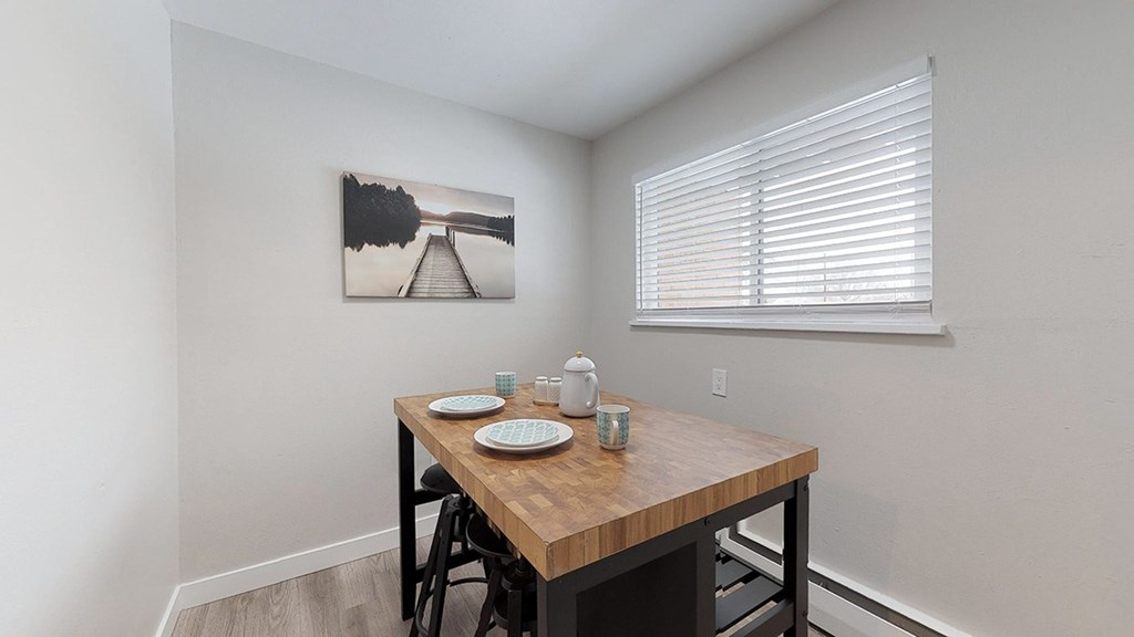 A dining table with four chairs and a painting on the wall.