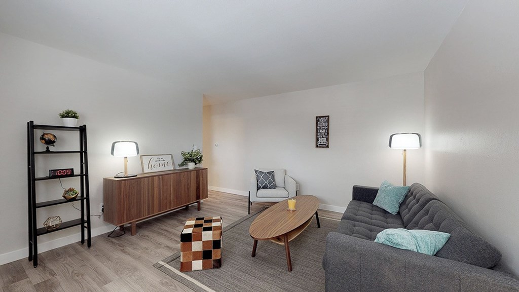 A living room with a grey couch, a wooden coffee table, and a wooden shelf with decorative items.