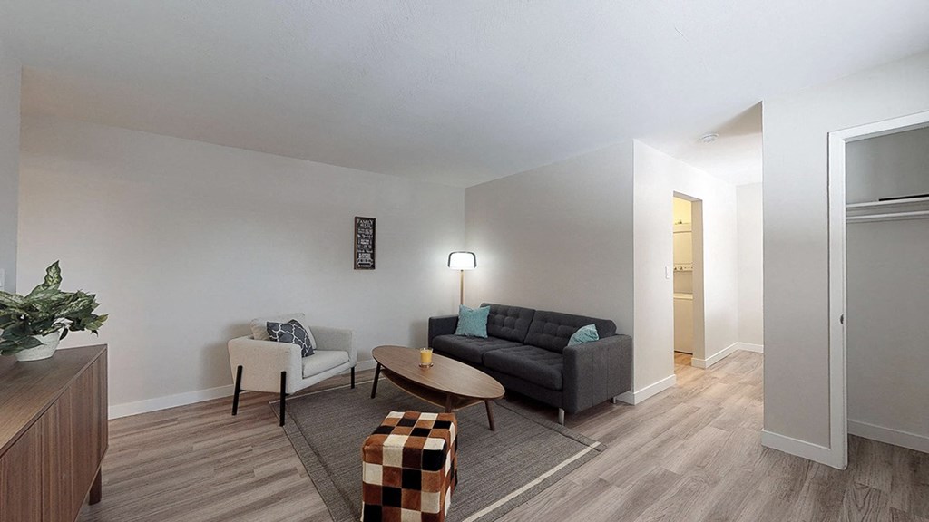 A living room with a black couch, a white chair, a coffee table, and a potted plant.