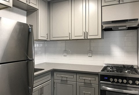 A kitchen with a stainless steel refrigerator and a stove with four burners.