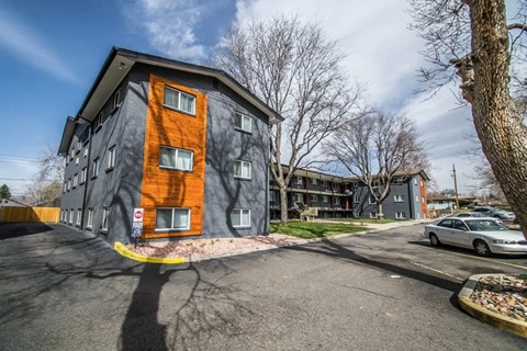 A modern building with a grey and orange facade is surrounded by a parking lot.
