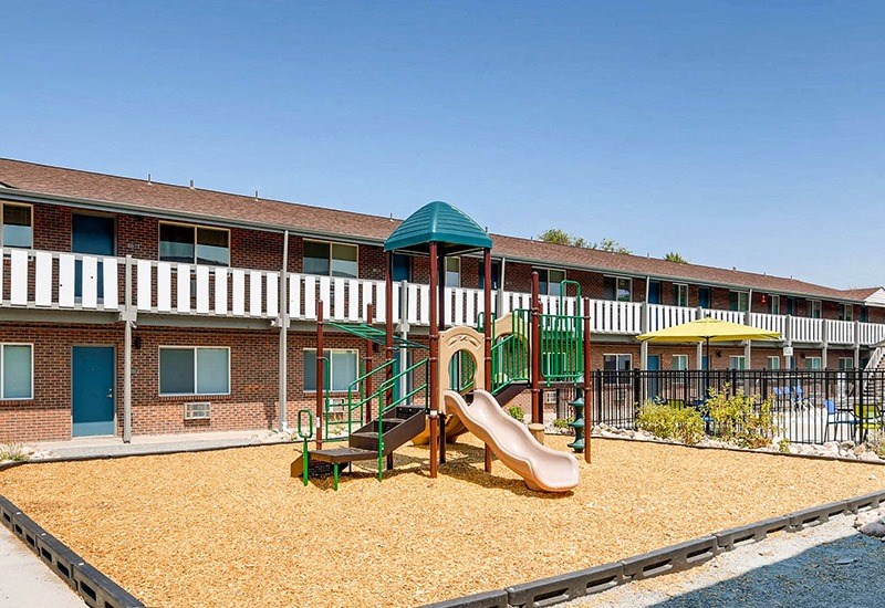 A playground with a slide and sandbox in front of a building.