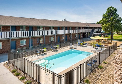 A black fence surrounds a small pool in front of a brick building.