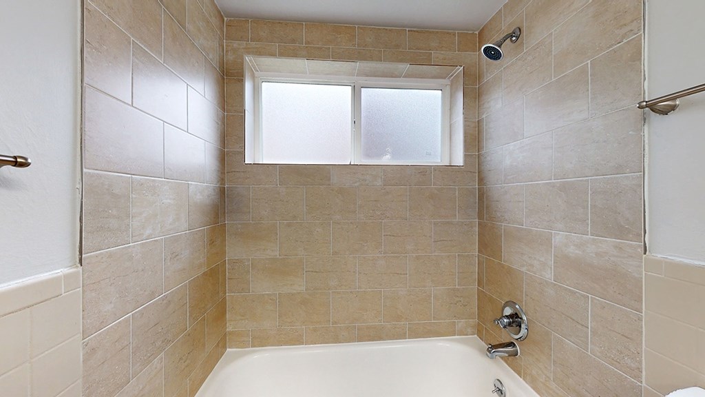 A bathroom with a tiled shower area and a window.