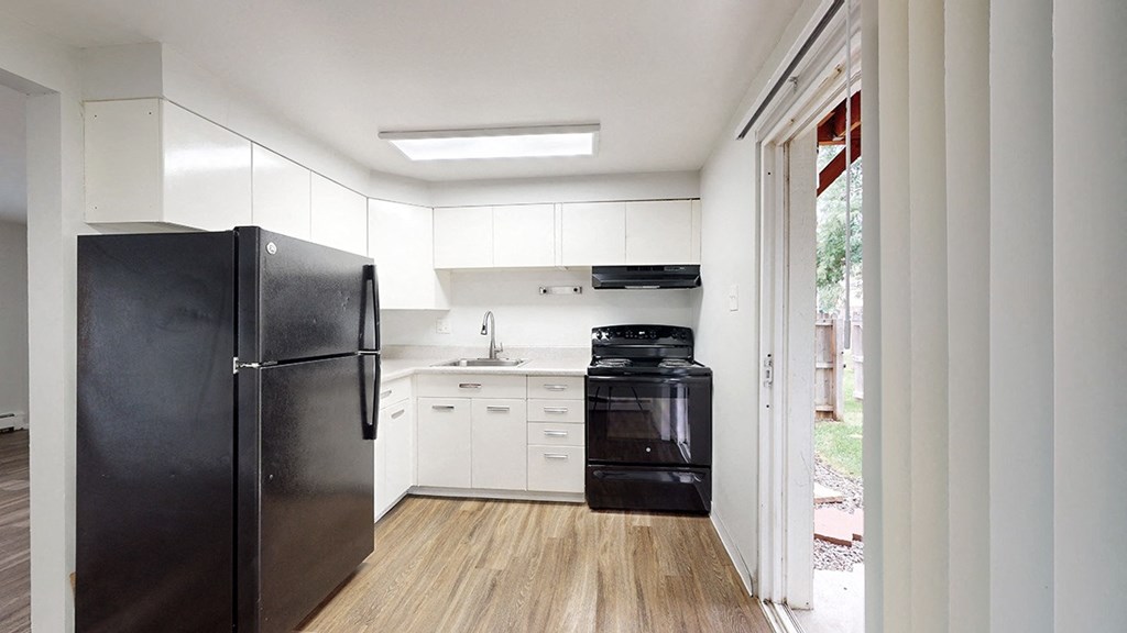A black refrigerator is in a kitchen with white cabinets.
