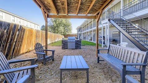 A wooden bench is situated on a gravel area under a wooden roof.