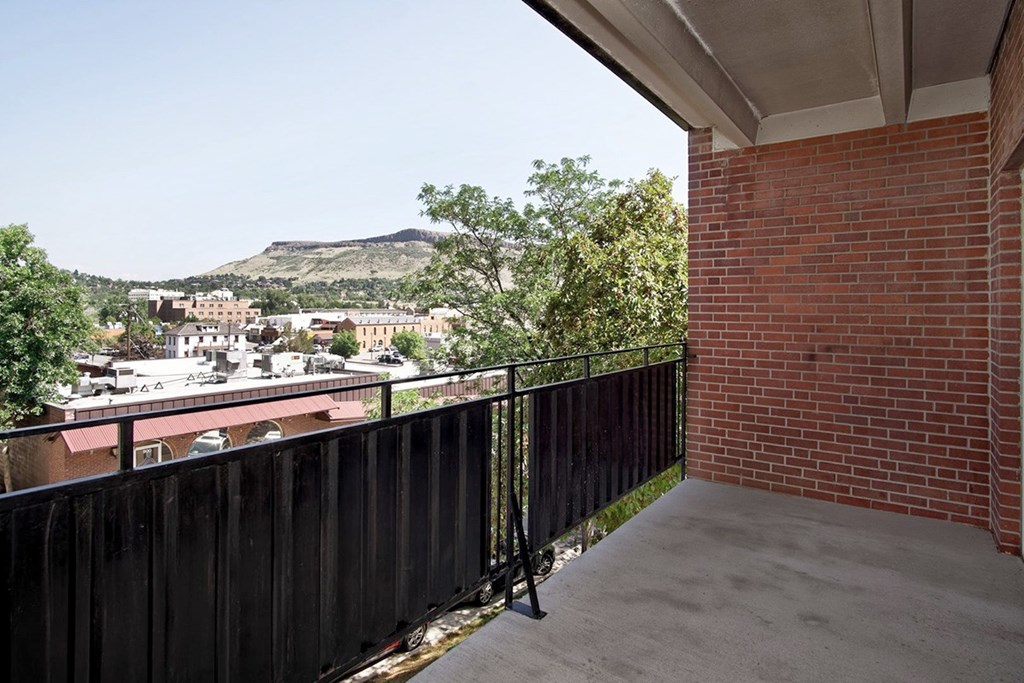 A balcony with a black railing overlooks a town with a mountain in the distance.