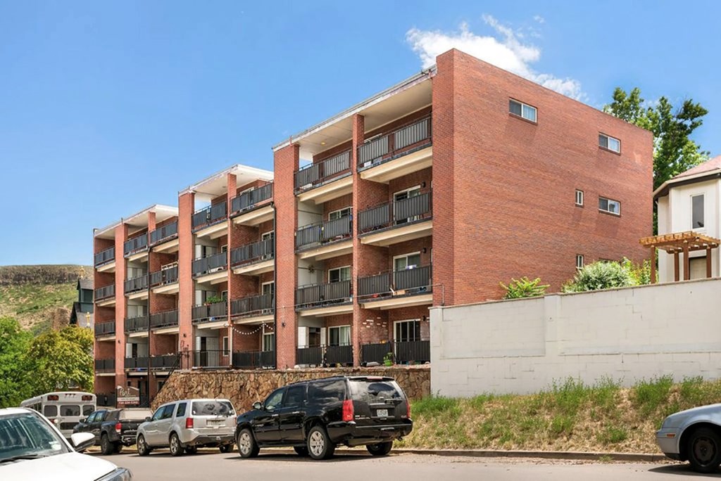 A red brick building with balconies and cars parked in front.