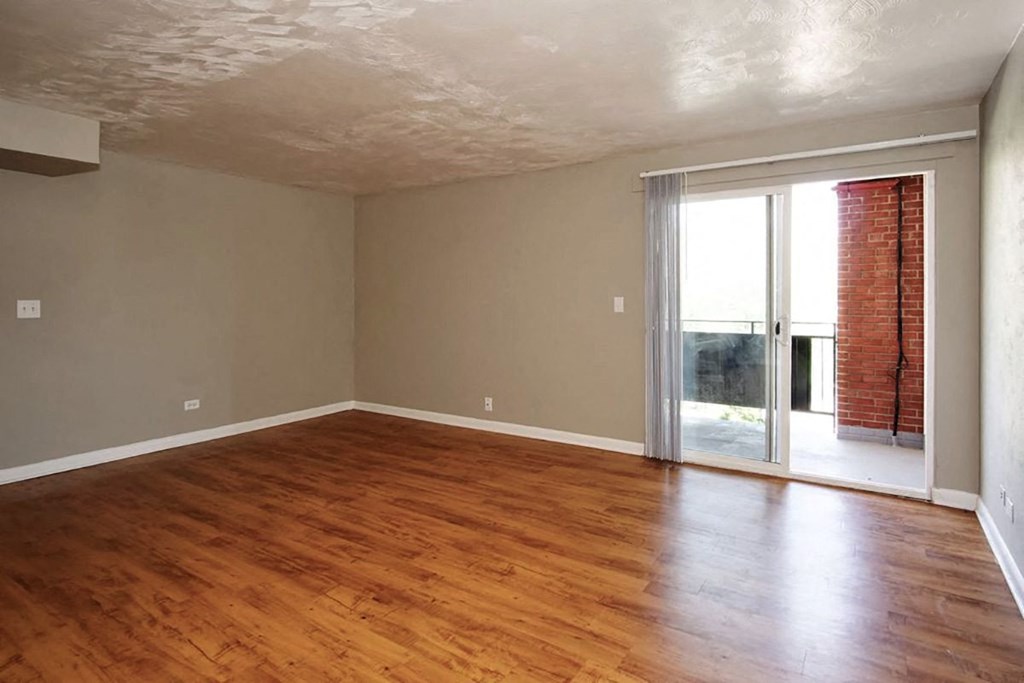 A room with wooden floors and a sliding glass door leading to a balcony.