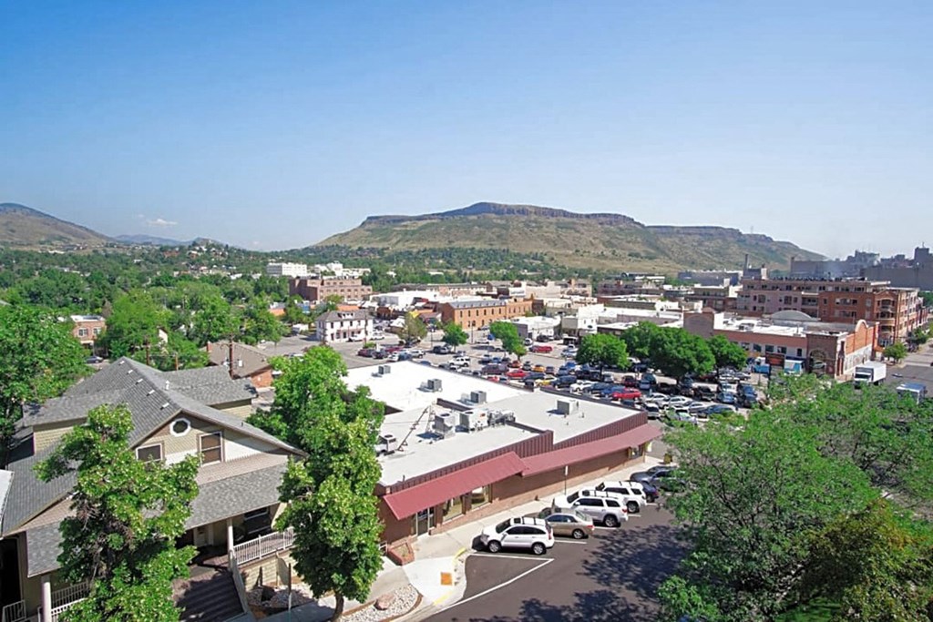 A parking lot with cars and a building in the foreground with trees and mountains in the background.