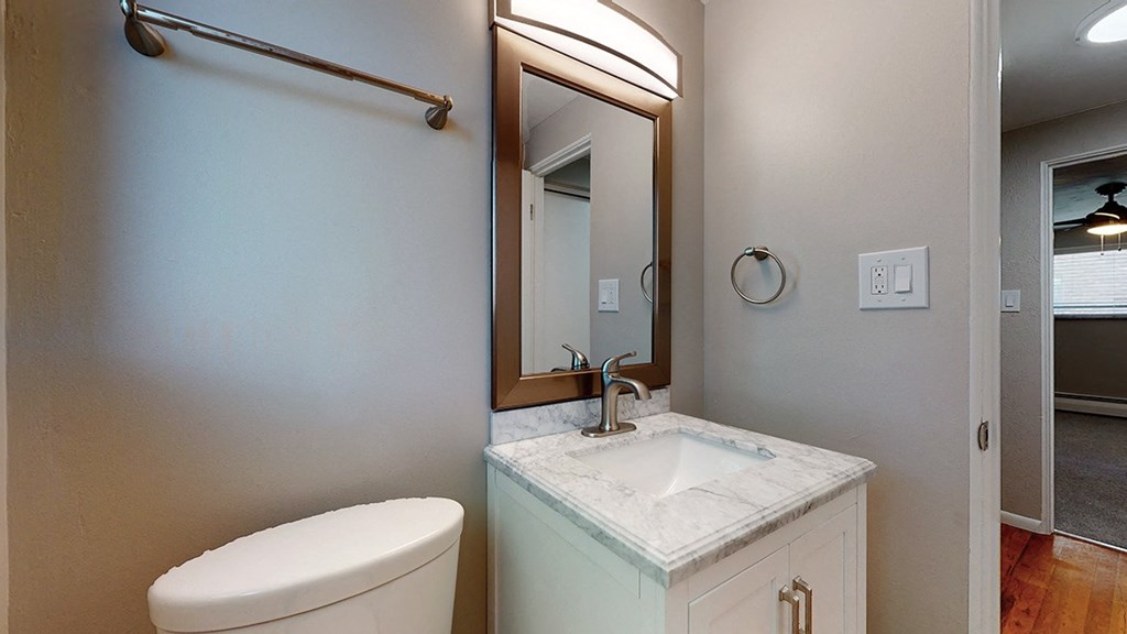 A bathroom with a toilet, sink, mirror, and light switches.