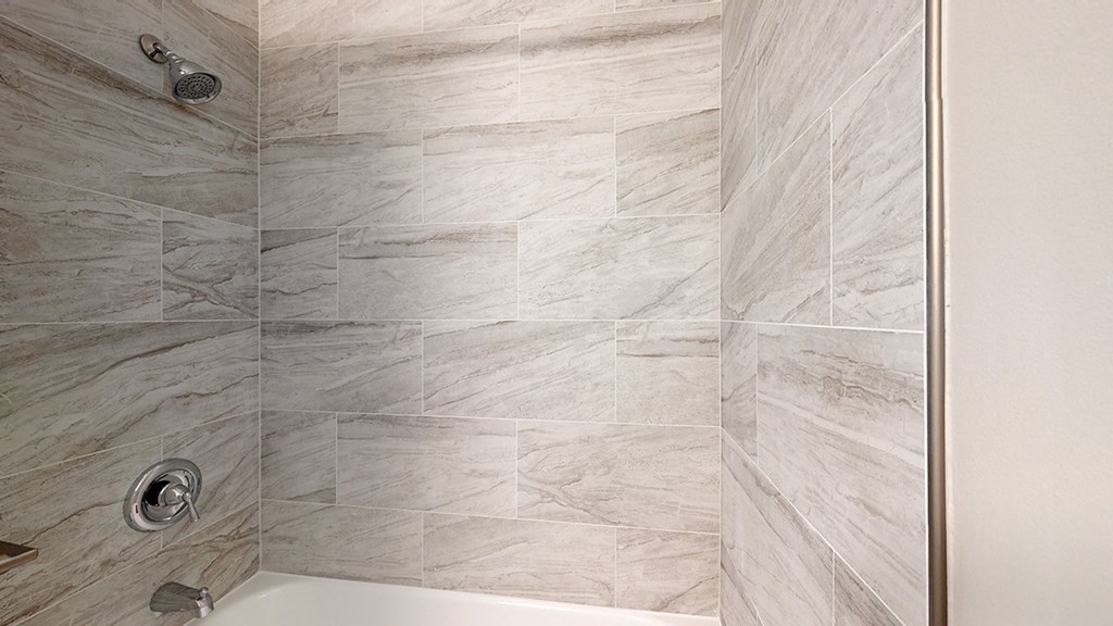 A shower with a tiled wall and a silver shower head.