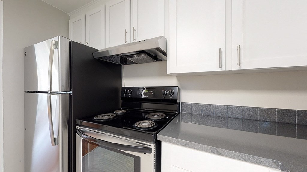 A black refrigerator is in a kitchen with a stove and oven under a vent.