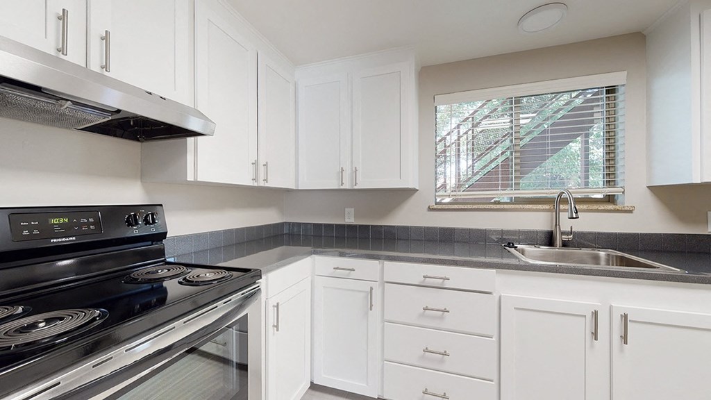 A modern kitchen with white cabinets and a stainless steel stove top.