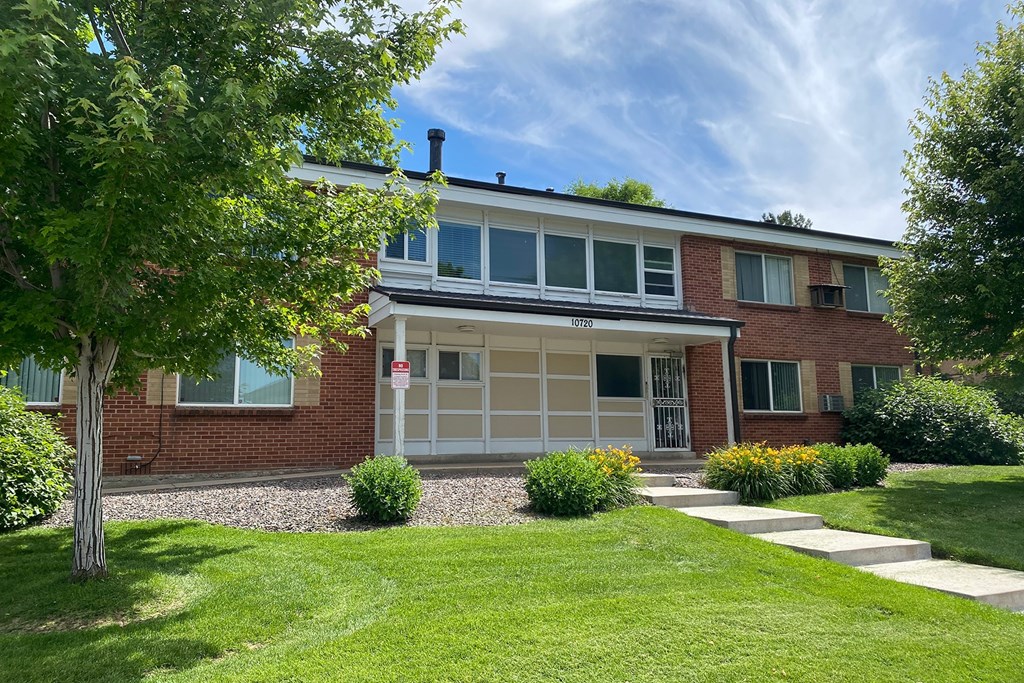 2-story red brick building with concrete steps leading to entry, landscaping and trees.