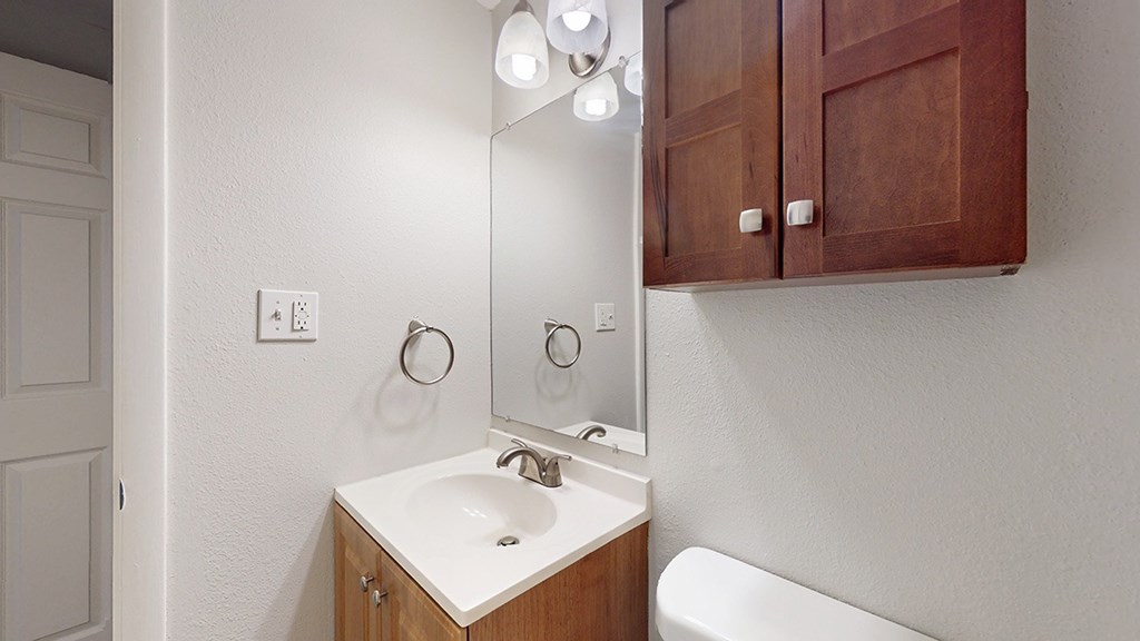 A bathroom with a white sink and brown cupboards.