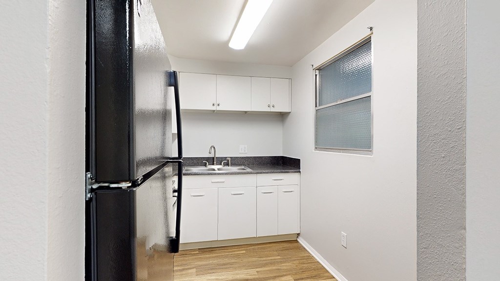 A black refrigerator stands in a kitchen with white cabinets and a black countertop.