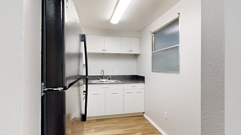 A black refrigerator stands in a kitchen with white cabinets and a black countertop.